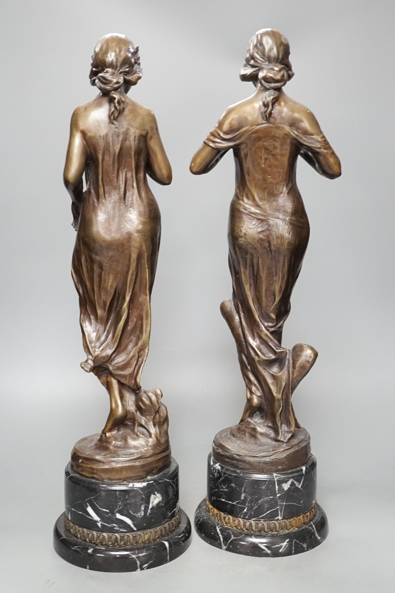 After Jean-Antoine Houdon, (French 1741-1828), a pair of bronze figures of lady’s holding flowers, on marble bases, 52cm